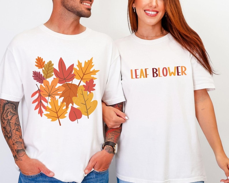 Couples matching fall shirts shown on man and woman. The man’s white tee has a graphic of layered autumn leaves in warm tones of orange, mustard yellow, and burgundy. The woman’s shirt reads “LEAF BLOWER” in bold block letters shaded in fall colors. Both stand side by side, smiling, styled in casual denim jeans. Perfect for autumn outfits, funny couple shirts, fall parties, Thanksgiving gatherings, and cozy seasonal photos.