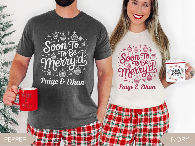 May include: Two people wearing matching Christmas shirts with the text "Soon To Be Merry'd" and the names "Paige & Ethan". The shirts are dark gray and ivory, with red and white text and ornaments. They are holding mugs.
