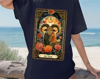 May include: A navy blue t-shirt with a graphic of an Aries zodiac sign. The graphic features a ram with horns, surrounded by flowers and a crescent moon. The text "Aries" is printed below the graphic.