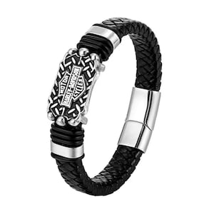 Op de afbeelding: Zwarte leren armband met een gevlochten ontwerp. De armband heeft een zilverkleurige metalen plaat met de woorden "MOTOR HARLEY-DAVIDSON CYCLES" en een zilverkleurige sluiting.