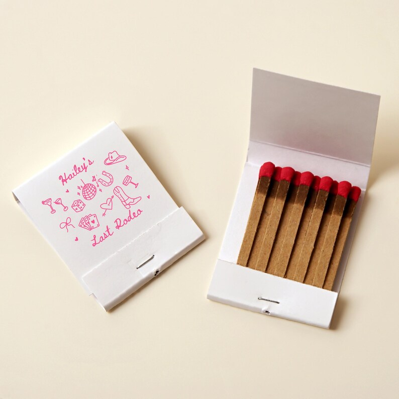 May include: A white matchbook with pink illustrations of party items and the text "Hailey's Last Rodeo". The matchbook is open to reveal a row of brown matches with red tips.