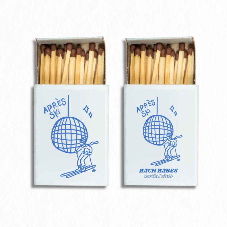 May include: Two blue and white matchboxes with a disco ball and skier graphic. The text on the boxes reads "Apr&egrave;s Ski" and "Bach Babes Social Club".