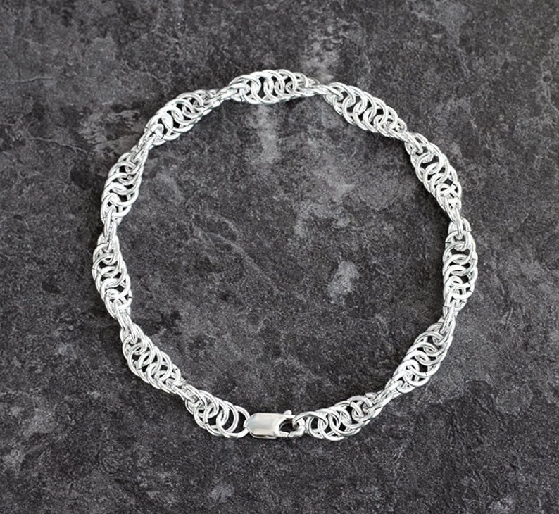 May include: A silver chain necklace with a unique, intricate design. The chain is made of small, interconnected rings that create a woven pattern. The necklace is approximately 18 inches long and has a lobster claw clasp.