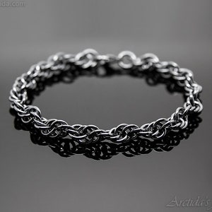 May include: A silver chain bracelet with a braided design. The bracelet is lying on a black surface.