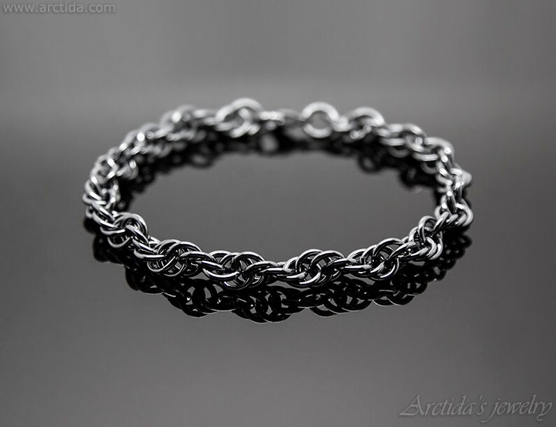 May include: A silver chain bracelet with a braided design. The bracelet is lying on a black surface.