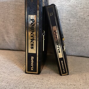 May include: Two black hardcover books with gold lettering and gold bookmarks. The books are titled "Powerless" and "Powerful" by Roberts.