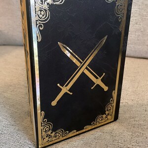 May include: Black book with a gold border and two crossed swords on the cover.