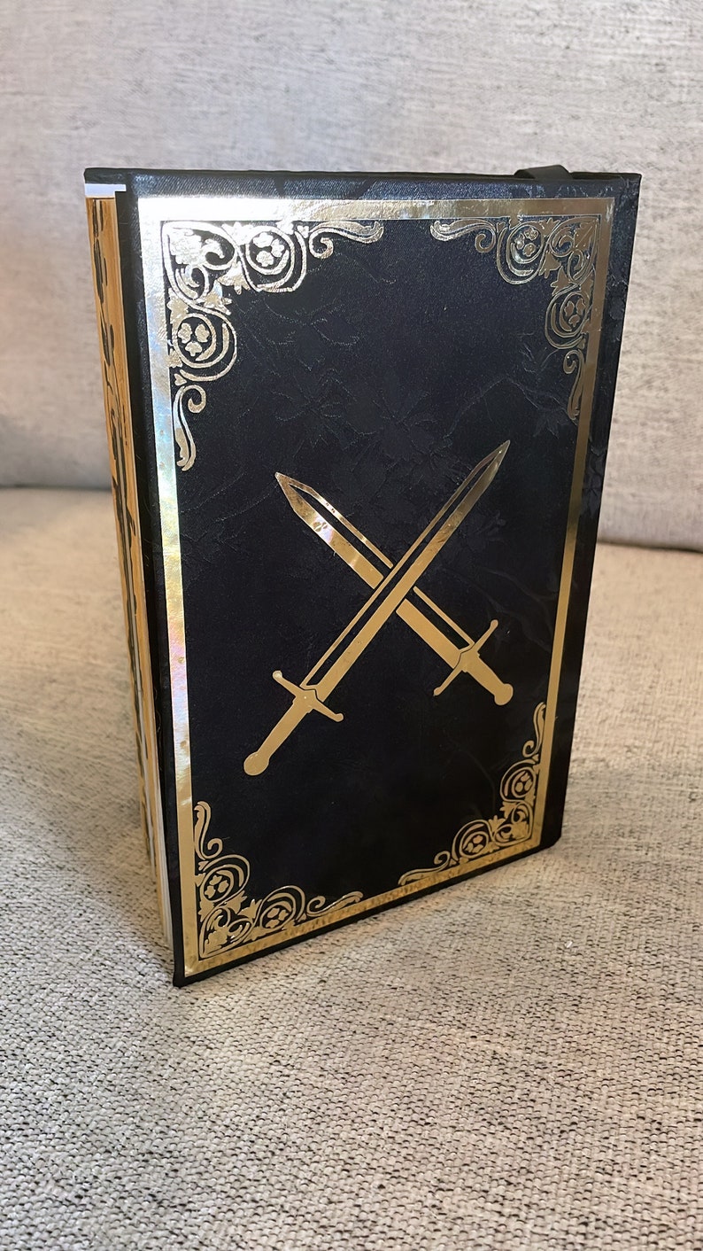 May include: Black book with a gold border and two crossed swords on the cover.
