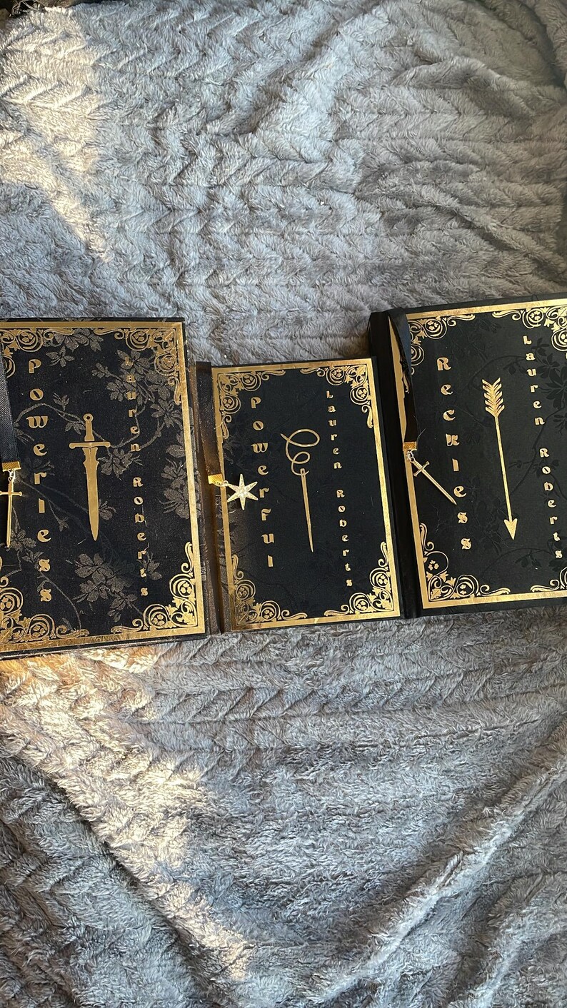 May include: Three black hardback journals with gold accents and decorative bookmarks. The journals are titled "Powerful", "Reckless", and "Brave".