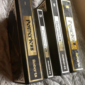 Op de afbeelding: Vier zwarte hardcover boeken met gouden letters. De titels zijn "Fearless", "Reckless", "Powerful" en "Powerless". Alle boeken zijn van de auteur Roberts.