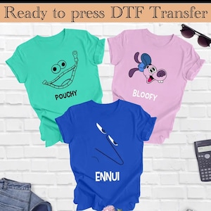 Op de afbeelding: Drie T-shirts met verschillende ontwerpen. Het eerste T-shirt is groen met een cartoon gezicht en de tekst "POUCHY". Het tweede T-shirt is roze met een cartoon hond en de tekst "BLOOFY". Het derde T-shirt is blauw met een cartoon gezicht en de tekst "ENNUI".