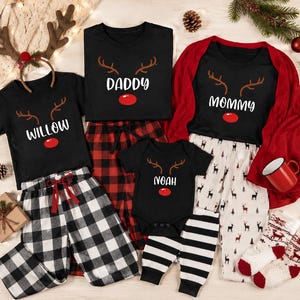 Pode incluir: Um conjunto de t-shirts pretas e um body com chifres de rena, um nariz vermelho e os nomes Willow, Daddy, Mommy e Noah. O conjunto inclui calças pretas e brancas aos quadrados, calças brancas com padrão de rena e calças pretas e brancas às riscas.