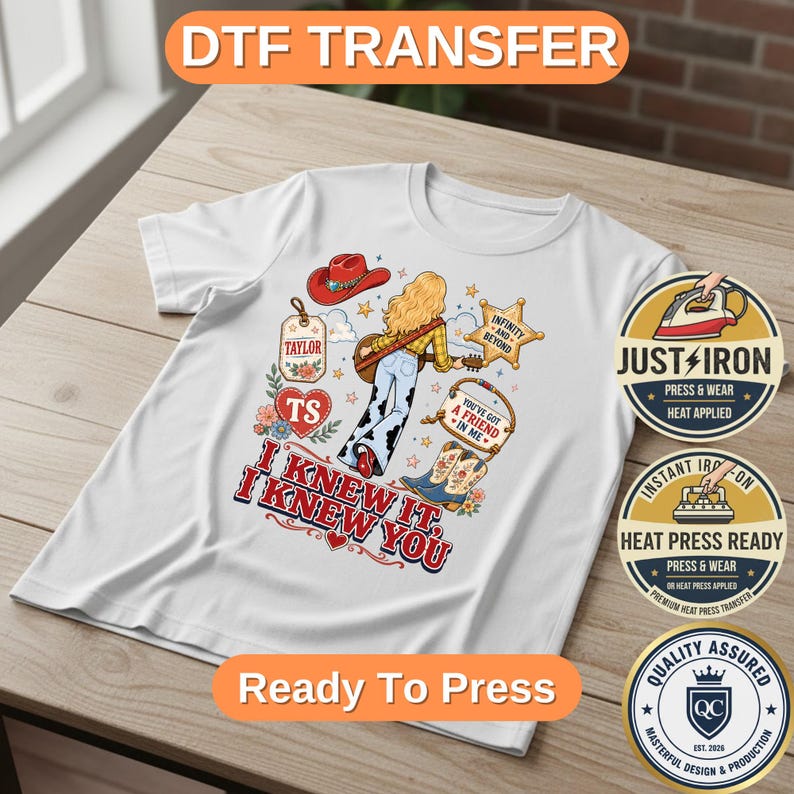 May include: A white t-shirt featuring a graphic print of a person with blonde hair, a red cowboy hat, a guitar, and cow-print pants. The design includes a sheriff star, a heart, and the text I KNEW IT, I KNEW YOU, TAYLOR, and A FRIEND IN ME.