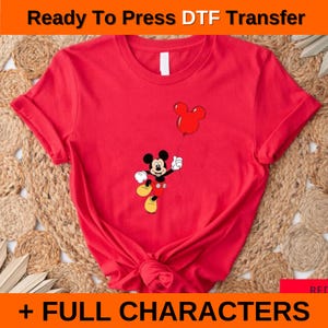 May include: Red t-shirt featuring a graphic of Mickey Mouse holding a red balloon. The shirt has rolled-up sleeves and a knotted front. Text at the top reads "Ready To Press DTF Transfer" and at the bottom "+ FULL CHARACTERS".