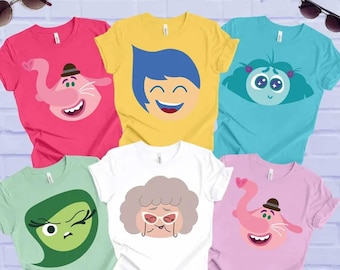 Op de afbeelding: Zes verschillende T-shirts met verschillende cartoonfiguren uit de film Inside Out. De personages zijn Joy, Sadness, Disgust, Fear, Anger en Bing Bong. De shirts zijn allemaal wit, met de personages in kleur op de voorkant gedrukt.