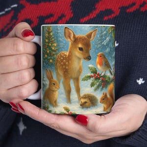 May include: White ceramic mug featuring a winter scene with a fawn, rabbit, robin, squirrel, and hedgehog. The design includes a Christmas tree and snowy background, creating a festive holiday theme.