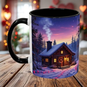 May include: White ceramic mug with a black rim and handle. The mug features a winter scene with a cozy cabin in the woods, surrounded by snow and glowing hearts.