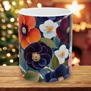 May include: A white ceramic mug with a floral design. The design features a variety of flowers in shades of orange, purple, blue, and white. The flowers are arranged in a random pattern and appear to be blooming in a garden.
