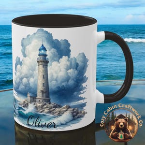 May include: White ceramic mug with a black rim and handle. The mug features a watercolor illustration of a lighthouse with a stormy sky and crashing waves. The name "Oliver" is written in black at the bottom of the mug.