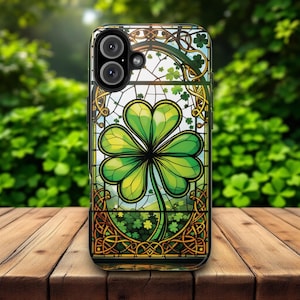 May include: A phone case with a stained glass design featuring a four-leaf clover in green and gold. The case has a black border and a cutout for the camera lens.