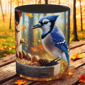 May include: A blue jay bird perched on a wooden bird feeder with a bowl of birdseed and nuts. The bird is looking to the left and has a blue crest and wings. The background is a blurred image of a forest with fall foliage.