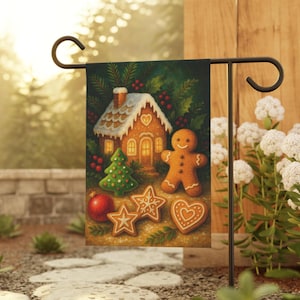 May include: A Christmas garden flag featuring a gingerbread house with a snow-covered roof, a gingerbread man, a Christmas tree, and various gingerbread cookies. The flag is displayed on a black metal stand in a garden setting.