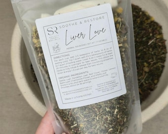 May include: A clear, sealed bag of herbal tea blend labeled "Liver Love" held by a hand. The bag contains dried herbs and flowers. The label includes directions and organic ingredients. The net weight is 1.7 oz (48g).