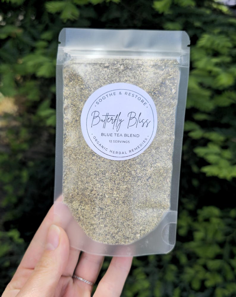 May include: A clear, resealable pouch filled with a blue tea blend. The pouch has a circular label with the text "Butterfly Bliss" and "Blue Tea Blend." The label also includes the phrases "Soothe & Restore" and "Organic Herbal Remedies."