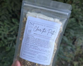 May include: A clear plastic bag containing a herbal tea blend. The label reads "Soothe & Restore Clear the Path Bitter Tea Blend." The bag contains dried herbs and roots. The net weight is 1.7 oz (50g).