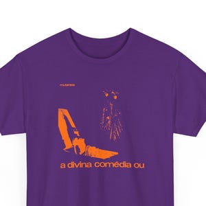 May include: Purple t-shirt with an orange graphic design and text. The design features abstract shapes and the words "a divina comédia ou". The word "mutantes" is above the design.