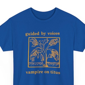 May include: Royal blue t-shirt with a gold graphic. The graphic features a stylized plant with four bat-like figures and the text "guided by voices" above and "vampire on titus" below.