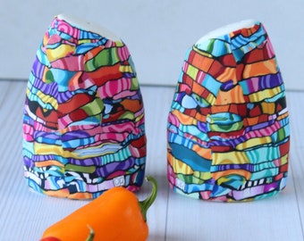 May include: Two colorful ceramic salt and pepper shakers with a geometric pattern in shades of blue, green, orange, red, and yellow.  Two red and orange chili peppers are in front of the shakers.