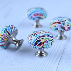 May include: Four colourful cabinet knobs with a white background. The knobs are round and have a silver base. The knobs are decorated with a colourful abstract pattern.