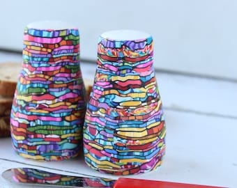 May include: Two colorful salt and pepper shakers with a geometric pattern in shades of pink, blue, green, yellow, and orange.