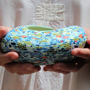 Peut inclure: Un bol en céramique avec un motif en mosaïque dans des tons de bleu, vert, rouge et blanc. Le bol a une forme arrondie et une finition lisse et brillante.