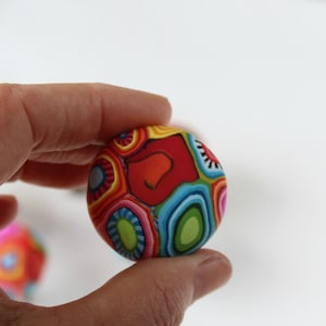 May include: A colorful, round, patterned bead with a red, yellow, blue, green, and white design.