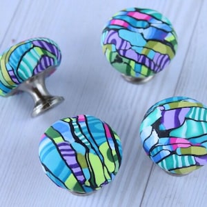 Peut inclure: Quatre boutons de cabinet abstraits à motifs colorés avec des bases argentées. Les boutons sont bleus, verts, violets et roses.