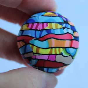 May include: A colorful, striped sphere made of polymer clay. The sphere is decorated with a variety of colors, including blue, pink, yellow, orange, and red.