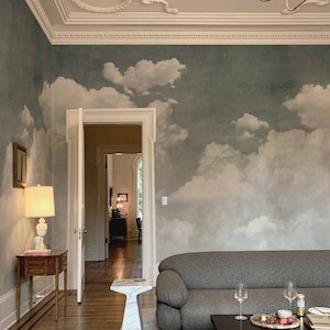 Könnte beinhalten: Ein Wohnzimmer mit einem grauen Sofa, einem weißen Marmor-Beistelltisch und einem schwarzen Couchtisch. Der Raum hat ein Wandbild mit Wolken an der Wand und eine weiße Decke mit verzierten Stuckleisten.