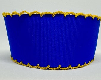 Op de afbeelding: Een helderblauwe, cilindervormige container met een getextureerd oppervlak. De boven- en onderranden zijn versierd met een decoratieve, geschulpte gouden rand. Het ontwerp van de container is eenvoudig maar opvallend.