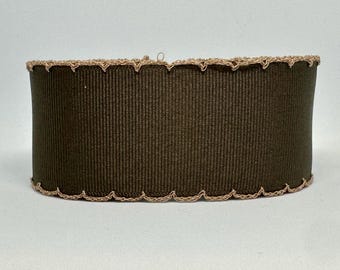Op de afbeelding: Een cilindrische lampenkap met een donkerbruine geribbelde stof. De boven- en onderranden zijn afgewerkt met een geschulpte, lichtbruine gehaakte rand. De lampenkap heeft een neutrale kleur en past bij vele interieurstijlen.