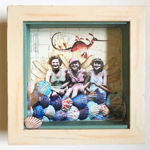 May include: Three women in vintage swimsuits sit on a bed of colorful seashells, with a seahorse and dragonfly wings behind them. The background is a vintage map.