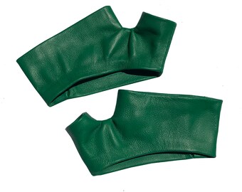May include: Two emerald green leather wrist cuffs. The cuffs are open at the top and have a textured surface. The cuffs are designed to be worn on the wrists.