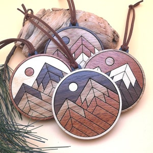 May include: Four wooden ornaments with a geometric mountain design and a moon. Each ornament is a different color of wood and has a brown leather cord.