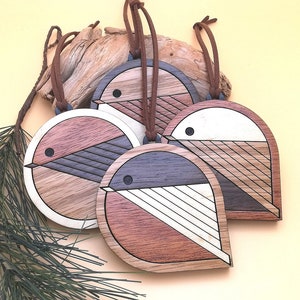 May include: Four wooden bird ornaments with geometric patterns in shades of brown, white and black. Each ornament has a brown suede cord for hanging.
