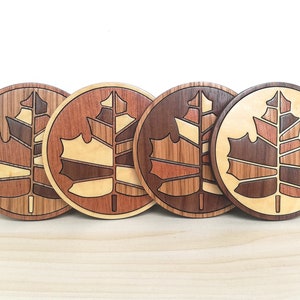 May include: Four wooden coasters with a maple leaf design. Each coaster features a different wood grain pattern, creating a unique and natural look.