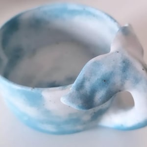 Könnte beinhalten: Eine blaue und weiße Keramik Schüssel in Form eines Wals mit einem Schwanzgriff. Die Schüssel hat ein marmoriertes Design.