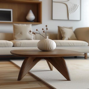 May include: A wooden coffee table with a unique, triangular base. The table is made of dark wood and has a smooth, oval-shaped top. A white ceramic vase with a ribbed design sits on the table, filled with dried branches.