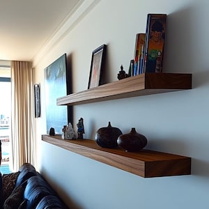 May include: Two floating wooden shelves mounted on a light blue wall. The top shelf holds framed art and books. The bottom shelf displays decorative vases and figurines. The shelves are made of dark wood.