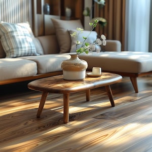 May include: A wooden coffee table with a natural wood finish and a rounded top. The table has four short legs and is sitting on a hardwood floor. A vase with white flowers and a small saucer with a cup are on the table.
